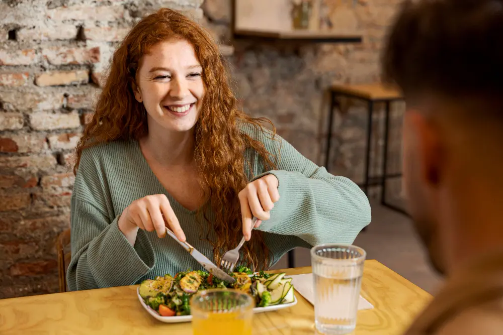 imagem de uma mulher sorrindo em um restaurante fazendo uma boa refeição saudável e nutritiva acompanhada por um homem